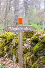 Trail marker for a hiking trail by a mossy stone wall in Sweden, Sweden, Europe