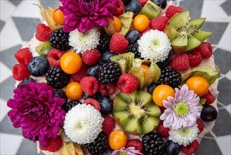 Delicious-looking cake garnished with a variety of berries and colourful flowers on a patterned