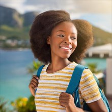 Cheerful woman with a backpack and afro hair in a striped shirt, basking in sunlight with a content