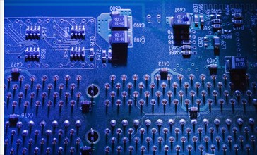 Close-up of blue lighted electronic computer circuit board with microchips and silver solder