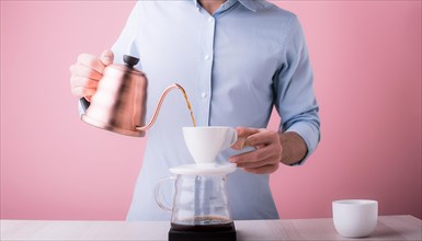 Man in blue shirt using a stainless steel kettle to brew coffee on a pink background, horizontal,