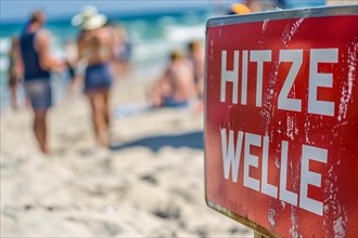 Warning sign with German text 'Hitzewelle' (Heat wave) in front of blurry sunny beach with people.