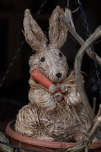 Straw wicker rabbit with carrot, sitting in front of a dark background as an Easter decoration,