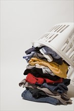 Close-up of white plastic laundry hamper or basket on top of pile of dirty clothes that includes