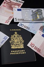 Close-up of five, ten, twenty Euro paper currency bank notes on top of Canadian passport on black
