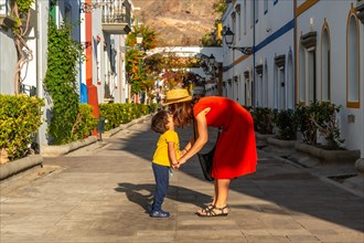 Mother in a red dress and her son walking in the port of the town Mogan in Gran Canaria. Family