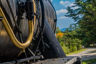 Side view of a vintage locomotive with blue sky, autumn trees, and mountains in the background, in