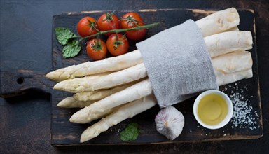Bunch of white asparagus on a wooden board with tomatoes, garlic and oil, bunch of white asparagus