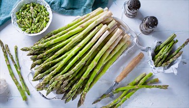 Green asparagus on a light-coloured base with salt shaker and pepper mill on the side, AI
