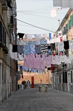 Colourful laundry hangs over a narrow alley between old houses, Venice, Veneto, Italy, Europe