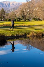 Male Golfer Reflected in a Water Pond and Hitting the Golf Ball on Fairway on Golf Course with
