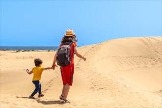 (Varios valores) Mother and son walking in the dunes of Maspalomas on vacation, Gran Canaria,