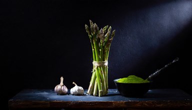 Asparagus and garlic cloves arranged on a stone board next to a bowl of powder, fresh green