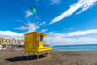 Yellow lifeguard tower in California with green flag in summer by the sea