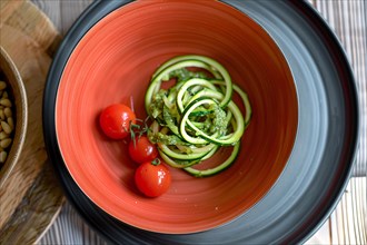 Healthy zucchini noodles with pesto and cherry tomatoes in a vibrant red bowl, AI generated