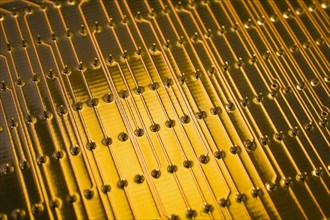Close-up of golden yellow lighted electronic computer circuit board with lines and silver solder