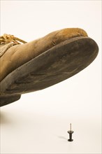 Close-up of elevated old and worn safety work shoe about to step on black upright pushpin with
