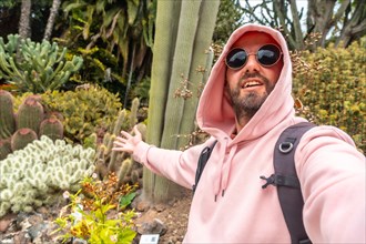 A smiling tourist enjoying in a tropical botanical garden with many captus