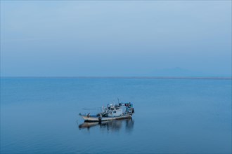 A solitary fishing boat rests on a tranquil sea under a gradient blue twilight sky, in South Korea