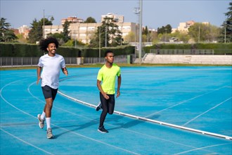 Two african american young sports men running together in an outdoor track