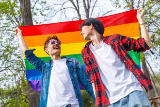 Low angle view portrait of a gay male friends raising lgbt rainbow flag in a park