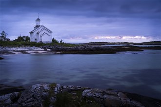 The white church of Gimsoy (Gimsoysand Church) by the sea, rocks in the foreground. At night at the