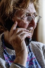 Laughing senior citizen with smock talking on the phone at home in her living room, Cologne, North