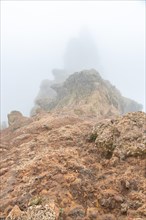 A rocky hillside with a foggy sky in the background. The fog is thick and the rocks are jagged and