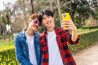 Young happy multi-ethnic gay couple taking a selfie together in a park