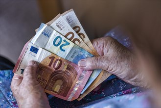 Senior citizen with wrinkled hands counts her money at home in her flat and holds banknotes in her