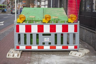 Construction site with barrier and waste container or skip for building rubble on a footpath,