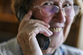 Laughing senior citizen talking on the phone at home in her living room, Cologne, North