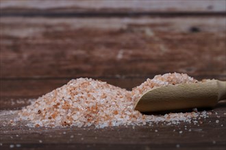 Close-up of a pile of pink himalayan salt in a wooden spoon on a wooden table with copy space