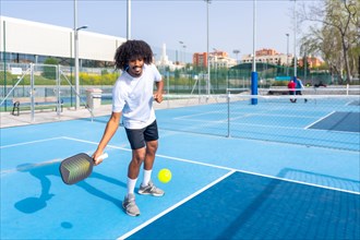 Full length photo of an smiling man with afro hair serving while playing pickleball in an outdoor