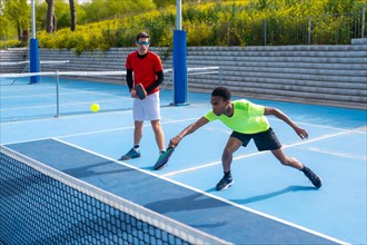 African man trying to reach the ball playing pickleball with a caucasian male partner in an outdoor