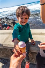 A young boy is holding an ice cream cone and giving it to another person. The scene is set on a
