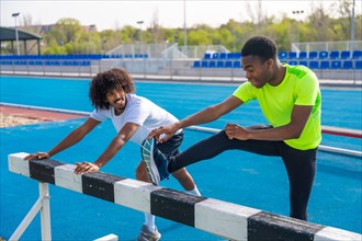 Two young african american sportsmen talking distracted while stretching legs in a running track