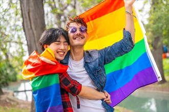 Happy multi-ethnic gay couple celebrating love waving lgbt flag in a park