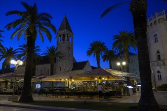 Outdoor restaurant at night with historic church tower and palm trees, Trogir, Dalmatia, Croatia,