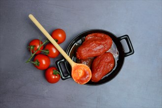Whole tinned tomatoes in a pot, tomatoes and wooden spoon