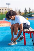 Vertical photo of an african american smiling runner tying the shoelaces getting ready to work out