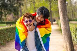 Multi-ethnic gay men wrapping in lgbt flag piggybacking in a park