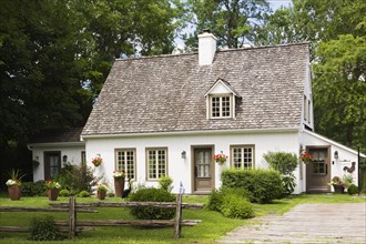 Old circa 1886 white with beige and brown trim Canadiana cottage style home facade in summer,