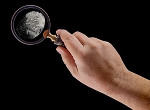 Male hand holding magnifying glass viewing A fingerprint on a black background