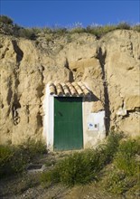 A green door built into a rock face under a clear blue sky, cave dwelling, Valtierra, Navarra,