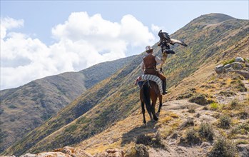 Traditional Kyrgyz eagle hunter riding with eagle in the mountains, hunting on horseback, near