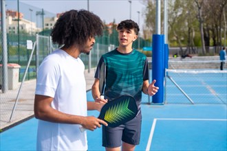 Caucasian young male instructor talking to a young african man playing pickleball in an outdoor