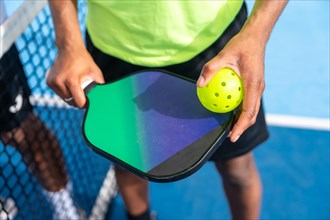 Top view close-up of man holding racket and pickleball ball standing in an outdoor blue court