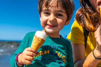 Mother with her little boy son enjoying summer vacation smiling eating ice cream by the sea