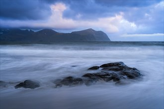 On the beach at Vikten. The sea washes around some rocks. Mountains in the background. At night at